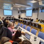 Participants in the conference room, working on laptops.
